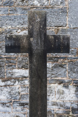 old grey concrete christian gravestone cross in front of stone wall background