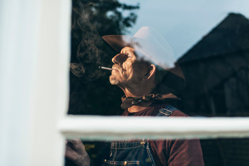 Farmer with beard and hat smoking cigarette standing behind wind