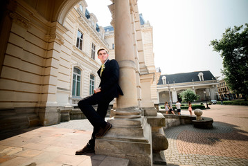 young and handsome groom in black suit standing near manor