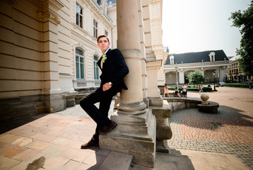 young and handsome groom in black suit standing near manor