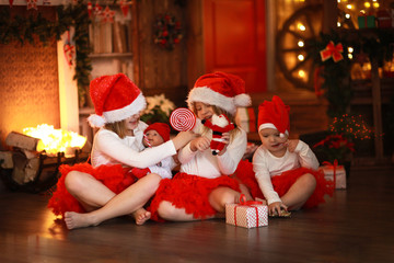 Siblings sisters in santa hats near  fireplace on Christmas ligh