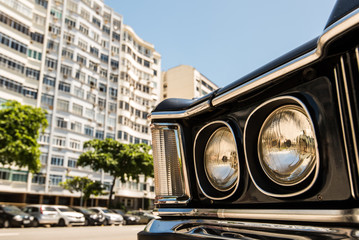 Headlight of a black classic American car with buildings in background