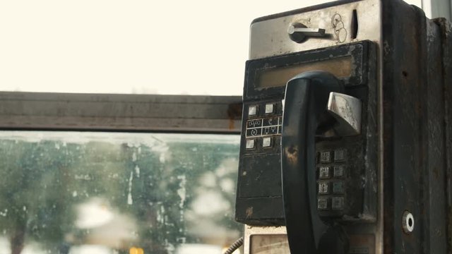 Old black rusty phone in phone booth coin. Close up.