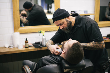 Obraz na płótnie Canvas Bearded man getting his hair and beard cut at the local barber s