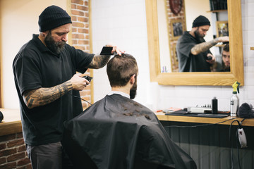 Bearded man getting his hair and beard cut at the local barber s