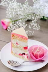 Homemade three layered cake with raspberry inside and pink candy on a white plate