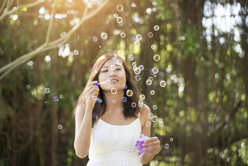 Beautiful woman wearing white dress blowing bubbles in the park,vintage style.