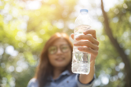 Beautiful woman wearing blue shirt and glasses, drinking water,holding bottom of drinking water in park.