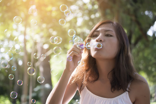 Beautiful woman wearing white dress blowing bubbles in the park,vintage style.