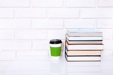 Fototapeta na wymiar Workplace with cup of coffee and books near brick wall on white table. Selective focus