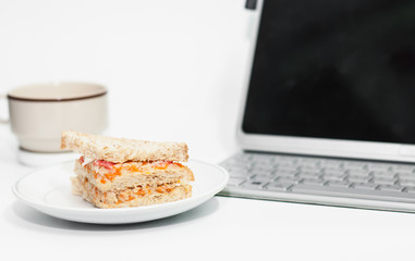Sandwich on dish put on white table,laptop and coffee cup on tab