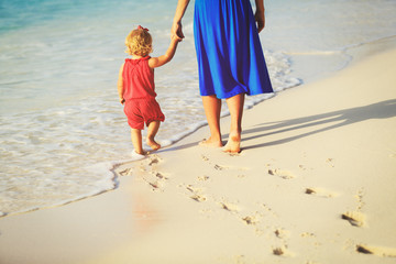 mother and daughter walking on beach leaving footprint in sand