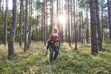 Obraz premium Young child boy (brother) giving his sister piggyback outdoors in the forest. Children summer activities.