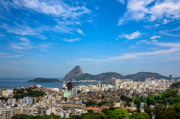 Obraz premium Urban view of Rio de Janeiro city with Sugarloaf Mountain, residential houses and a nearby slum favela adjacent to the hillside of Santa Teresa district