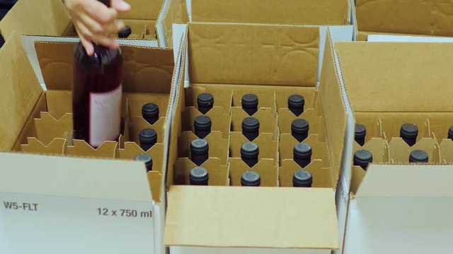 Packaging bottle with alcohol. Work puts bottle of wine in cardboard boxes