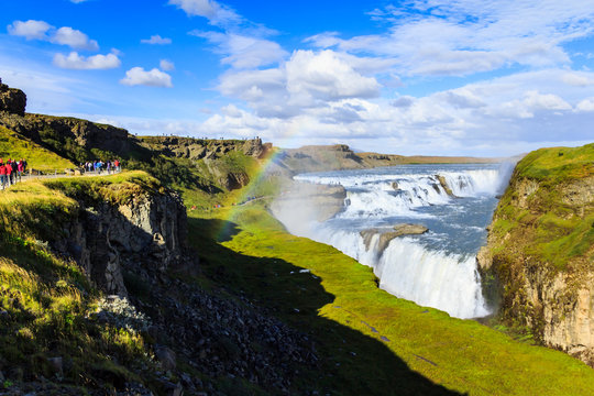 tourists watching rainbow on waterfall in Iceland