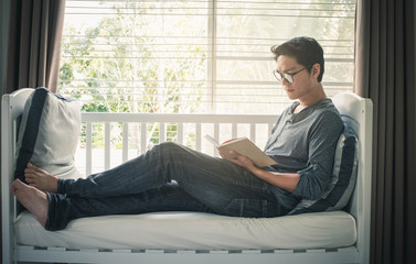 Man reading book on sofa. Lifestyle Relaxation Concept. Young man sitting on window sill and reading. handsome guy holding book and resting.