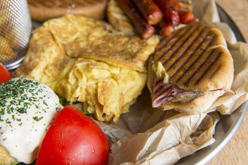 Breakfast set. Pan of scrambled eggs, grill sausages, tomato, fried potato wedges, salami sandwich, sour cream.