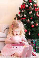 Девочка в розовом платье удивлённо открывает подарок