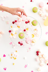 Top view of hand taking macaroon from plate with desserts