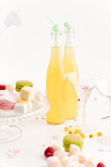 Two bottles of lemonade, glasses and macaroons on the table