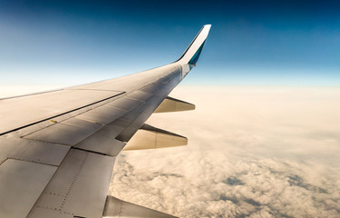 Fototapeta na wymiar window view of aircraft wing flying over clouds in blue sky (boeing 737)