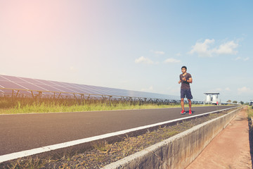 Obraz premium handsome man running on road with solar power plant in morning ;