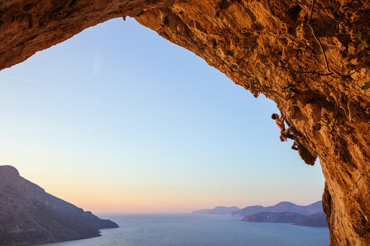 Young man climbing in cave at sunset