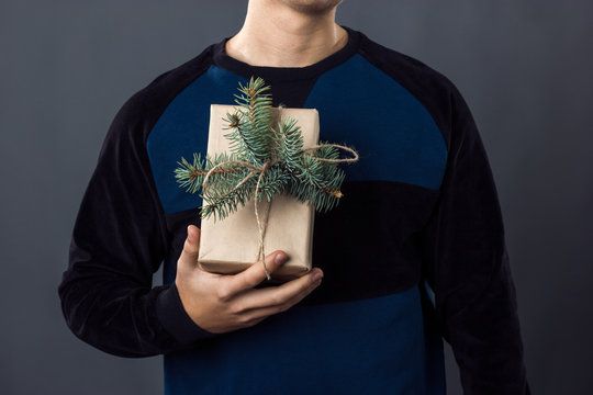 Handsome businessman holding gift box overwith a branch of Christmas tree  gray background