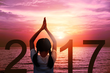 Happy new year card 2017. Silhouette of girl doing Yoga vrikshasana tree pose on tropical beach with fantastic sunset sky background. Kid standing as part of the Number 2017 sign and watching sunrise.