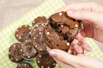 Hand of a woman holding a chocolate muffin open. Close up on a freshly baked cacao muffin with candy on top.