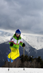 Young skier jump with ski poles in sun winter mountains