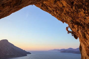 Foto auf Acrylglas Young man climbing in cave at sunset © Andrey Bandurenko
