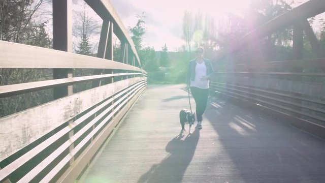 Dolly Shot of Pregnant Woman Walking Dog Across Bridge with Sun Flares