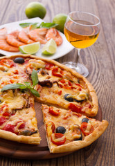Big tasty pizza with seafood, tomatoes, wine on wooden table