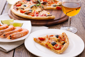 Big tasty pizza with seafood, tomatoes, wine on wooden table