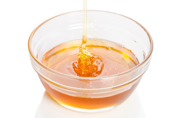 Honey dripping into glass bowl isolated on white background