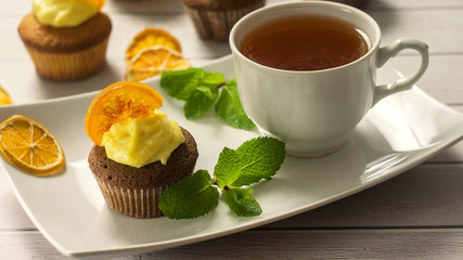 Obraz na płótnie Canvas Tasty cupcakes with caramelized orange, mint and cup of tea close-up