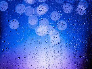 Window with rain drops, bokeh ligths and blue purple color