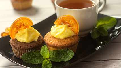 Tasty cupcakes with caramelized orange, mint and cup of tea close-up