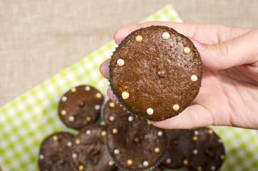 Hand of a woman holding a chocolate muffin. Close up on a freshly baked cacao muffin with candy on top.