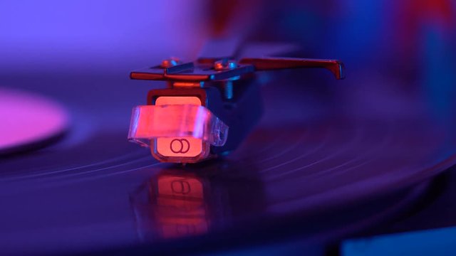 The needle drops on the disc, macro. Vinyl disc turning on retro record player.