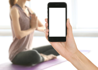 Female hand with smartphone. Woman practicing yoga, blurred background