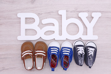 Different baby shoes and word BABY on wooden floor, top view