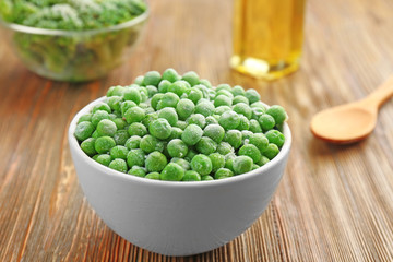 Frozen peas in bowl on wooden background