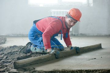 worker screeding indoor cement floor with screed