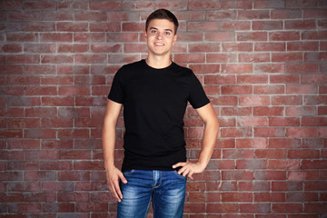 Handsome young man in blank black t-shirt standing against brick wall