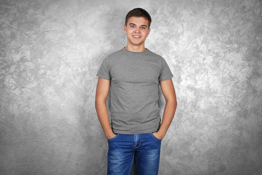 Handsome young man in blank grey t-shirt standing against textured wall