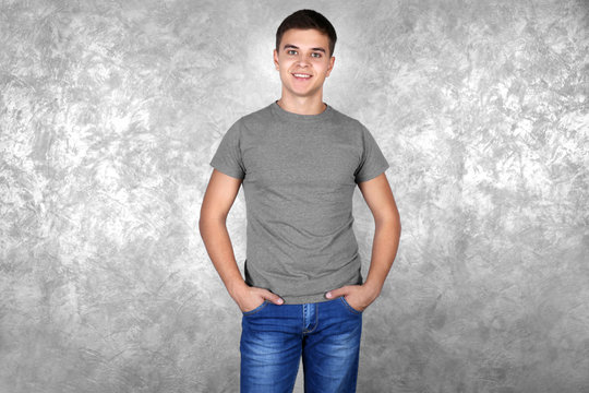 Handsome young man in blank grey t-shirt standing against textured wall