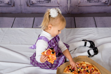 The child, a little girl sitting on the floor and having fun eating pizza. Unhealthy diets.